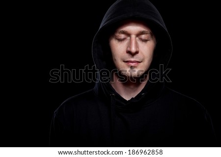 Young curly hair caucasian man wearing black hooded sweatshirt. Low key portrait taken on black background.