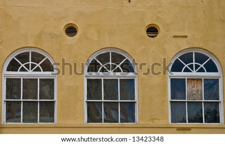 Three windows in an old building with vents and boarded pane