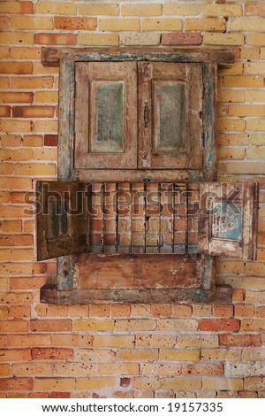 Old rustic wooden cabinet hanging on a brick wall, with opened lower doors showing bars