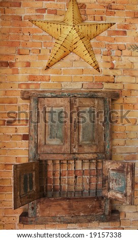Old rustic wooden cabinet hanging on a brick wall, with opened lower doors showing bars and yellow metal country star