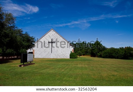 Old church in large field with empty sign and cross on side of building