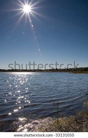 Sun with lens flare over a lake with small bit of shore in corner