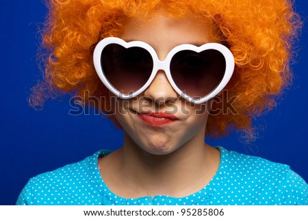 Beautiful young girl with orange party wig over blue background