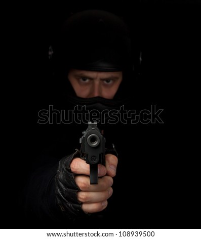 Armed assassin with motorcycle helmet aiming into the camera against a black background