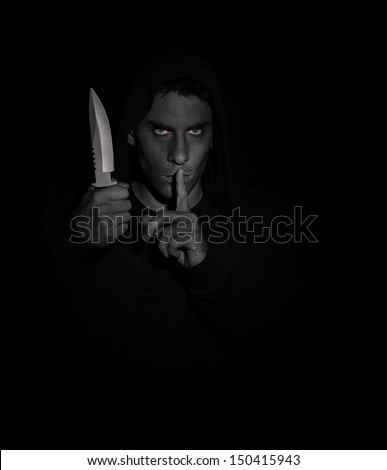 Evil man gesturing silence while holding a knife. Black and white, eyes in color