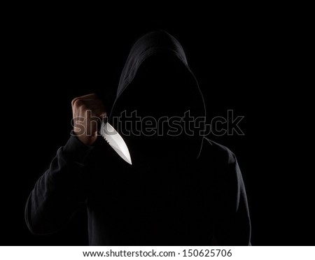 A dangerous hooded man standing in the dark and holding a shiny knife. Face can not be seen