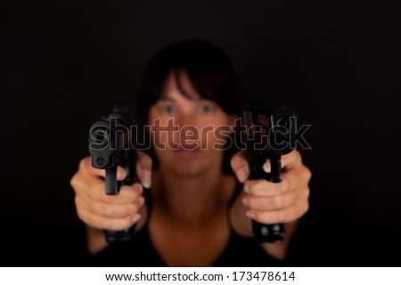 Woman aiming two guns against a dark background. With focus on the guns