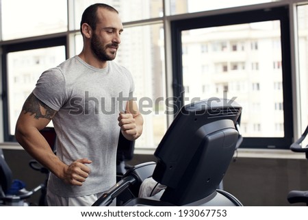 Muscular man running on a treadmill in a fitness club, sport in the fitness club