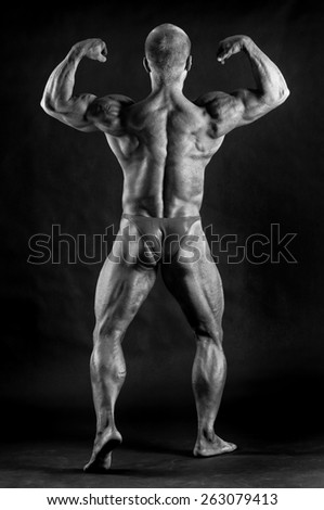 The muscular male bodybuilder flexing biceps on black background