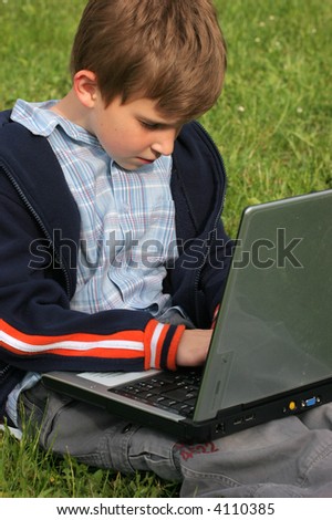Child is sitting with laptop in the park