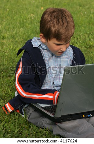 Child is sitting with laptop in the park