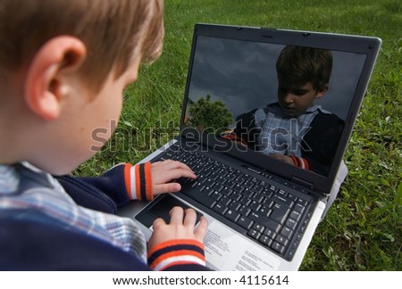 Child is sitting with laptop  in the park his face is mirorred on the screen