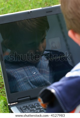 Child is sitting with laptop  in the park his face is mirorred on the screen