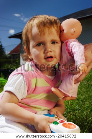 Young girl child outdoor sitting on the grass and get kiss from the doll