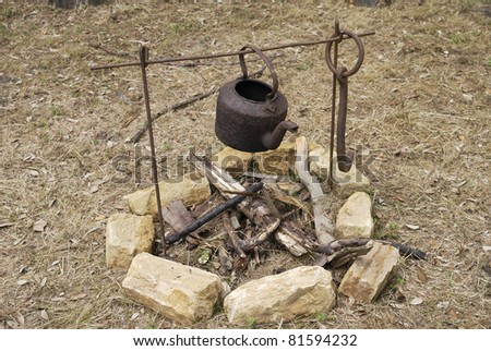 Old rusty kettle on iron frame over an unlit open fire outside in countryside