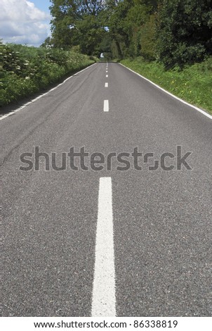 Straight tarmac country road with white lines on edge of woodland in West Sussex. England