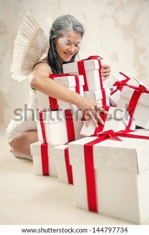 Beautiful young woman as angel with heap of gift boxes posing indoors