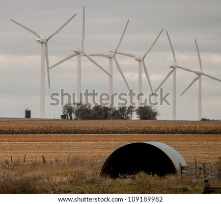 A wind farm and farmland with crop coexist. Windmills generating green energy on a cloudy day.