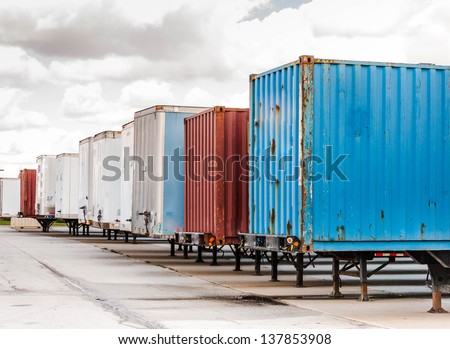 Shipping containers and semi truck trailers waiting in parking lot at huge loading dock