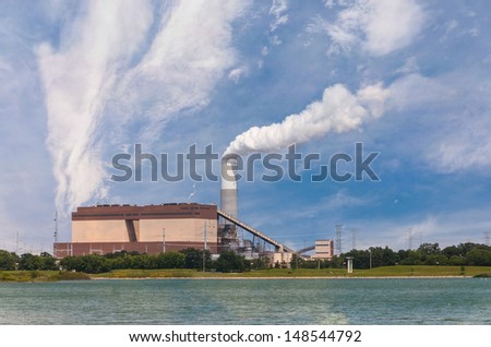 Coal powered power plant on bank of a river spewing pollution in the air, with natural gas generators as backup