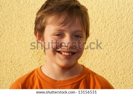 The  child dressed in orange T-shirt, at the rear of his yellow background. A smile is open, visible teeth.