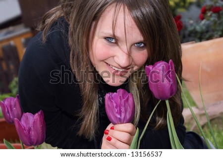 Teenage girl sitting on beds with flowers, she dug smiles, breathe the smell of tulips.