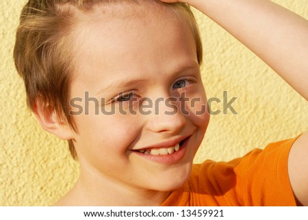 The  child dressed in orange T-shirt, at the rear of his yellow background. A smile is open, visible teeth.