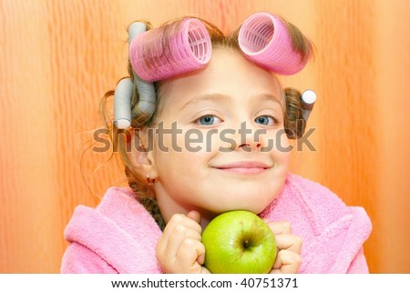 Girl in a pink housecoat, with curlers in the head and the apple of her face, isolated on orange background.