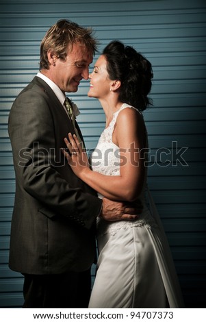 Bride and Groom touching noses against a blue wall and laughing