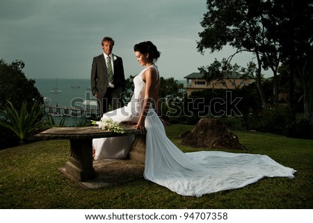 Bride sitting with dress stretched out behind and husband in the background
