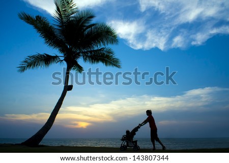 silhouette of mother pushing the stroller and walking on the sunset beach