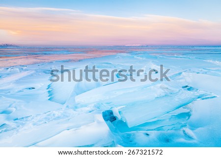 Transparent block of ice under orange sunset sky. Baikal lake, Russia