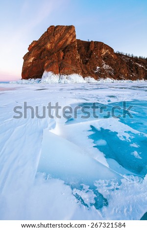 Transparent block of ice under orange sunset sky. Baikal lake, Russia