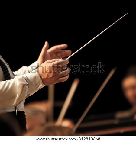 The hands of the conductor on the background of the orchestra in dark colors