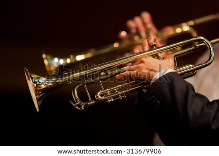 Hands of man playing the trumpet in the orchestra in dark colors