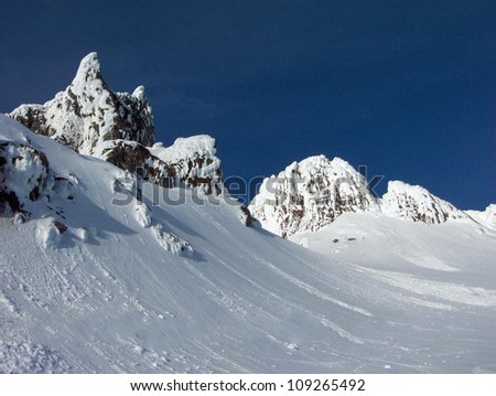 Summit of Mt. Hood in the State of Oregon, high mountain peaks with black rocks, jagged formations, snow covered hills and blue sky.