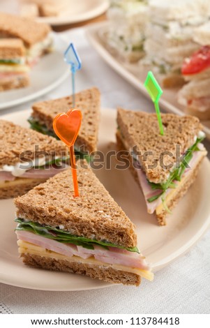Group of tea sandwiches with  cheese, ham and lettuce on a plate