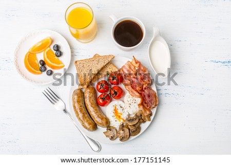 Healthy Full English Breakfast -  plate with poached eggs, sausages,  mushrooms, toasts and bacon, fruit, cup of fresh coffee and orange juice on white background