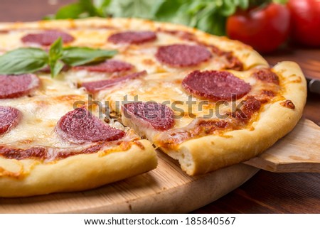 Slice of Pepperoni Pizza  being removed from whole pizza with tomatoes in background