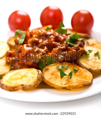 roasted country-styled potatoes with meat tomato sauce on a white plate and three cherry tomatoes at the back