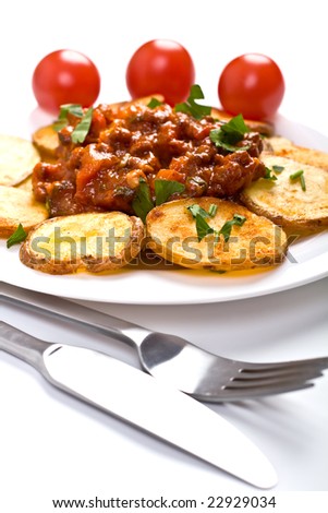 roasted country-styled potatoes with meat tomato sauce on a white plate, a fork and a knife and three cherry tomatoes at the back