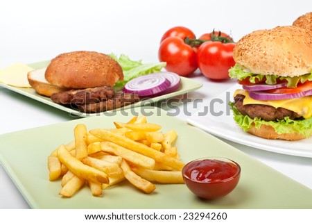 two big cheeseburgers and french fries with tomatoes and ingredients for another burger