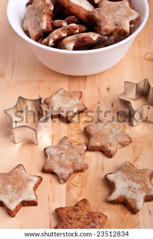 homemade star-shaped christmas cookies with a star cookie-form on a wooden board with more cookies in a bowl at the back