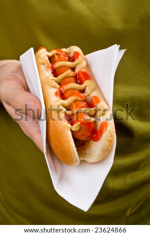 close up of a hot dog in a paper napkin being held in one hand