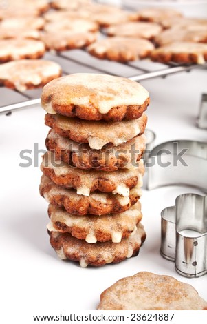 Stack of six Star Shaped Homemade Christmas Iced Cookies with a Cookie Cutter and More Cookies on a Railing on White Background