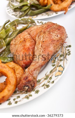 roasted chicken leg with onion rings and green beans on a plate