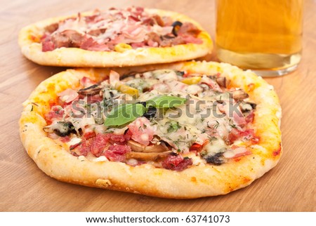 two meat and mushroom pizzas and a glass of beer on a wooden table