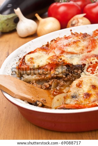 casserole dish with classic greek moussaka with eggplant, ground meat, potatoes, tomatoes baked with bechamel sauce and grated cheese