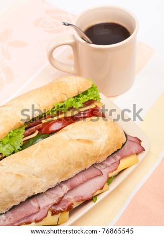 two  long baguette sandwich with lettuce, vegetables, salami and cheese and a cup of coffee
