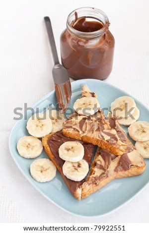 chocolate and peanut buttered toasts and pieces of bananas on a plate, an open chocolate spread container and a knife